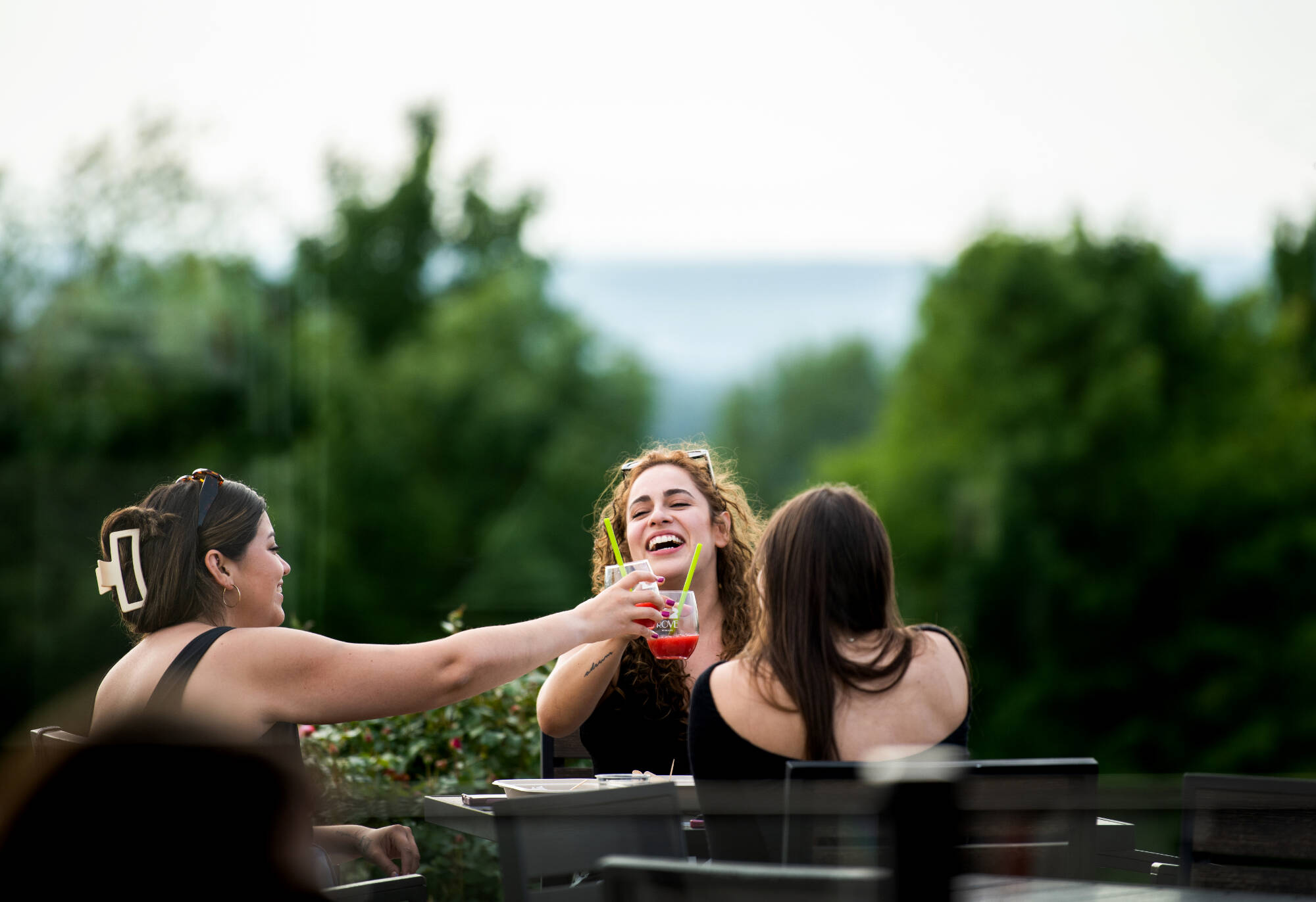 three women sitting at a table, toasting glass of drink with each other